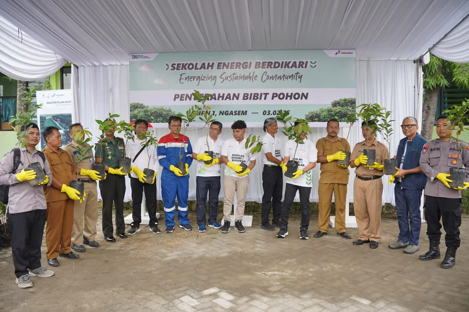 Beberapa perwakilan PT Pertamina EP Cepu (PEPC) Zona 12 berseragam pertamina, SMPN 1 Ngasem berseragam dinas coklat, beberapa orang memakai kaos putih bertuliskan 'sekolah energi berdikari dan beberapa orang lainnya berdiri berbaris di depan banner acara. Mereka memakai sarung tangan kuning dan membawa bibit pohon.