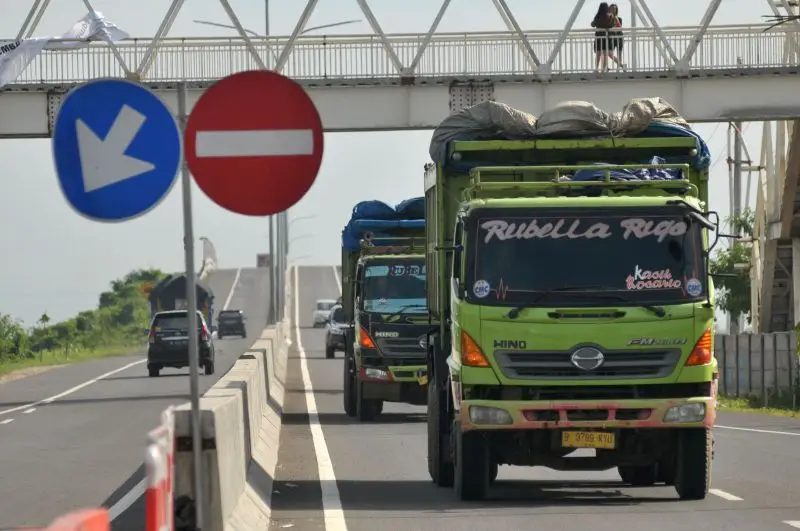 Truk di jalan tol difoto tampak depan, di sampik kirinya terdapat rambu stop.